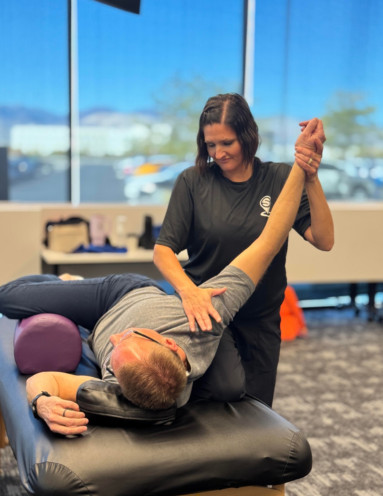 Practitioner stretching a client's hamstring on a table, bright studio light